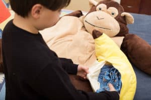 boy putting pajamas in stuffed banana bag with monkey sleeping bag