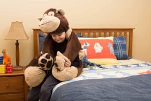 boy wearing stuffed brown bear as blanket on bed